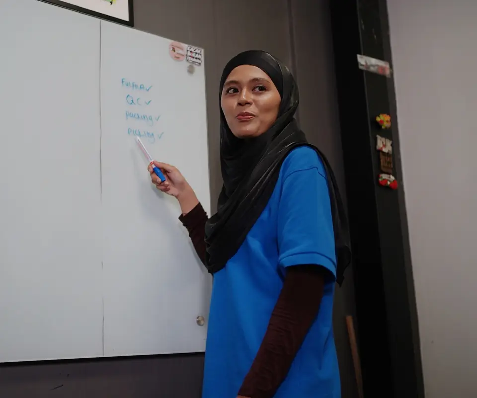 A FULFILA supervisor trains a team at a whiteboard listing QC, packing and picking